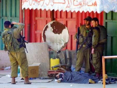 Israeli soldiers pose for pictures beside the body of a Palestinian gunman