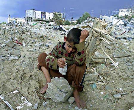A Palestinian boy sits atop the rubble of his home
