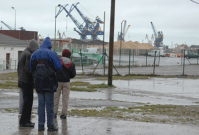 Three refugees huddle together under dockland cranes