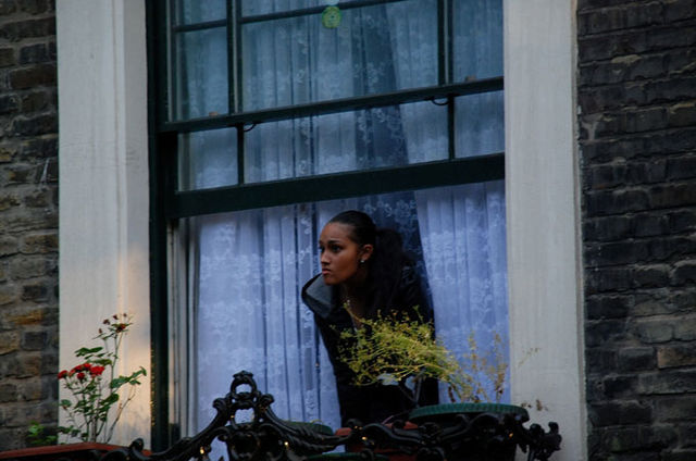 A young girl of about seventeen leaned anxiously out of her front window