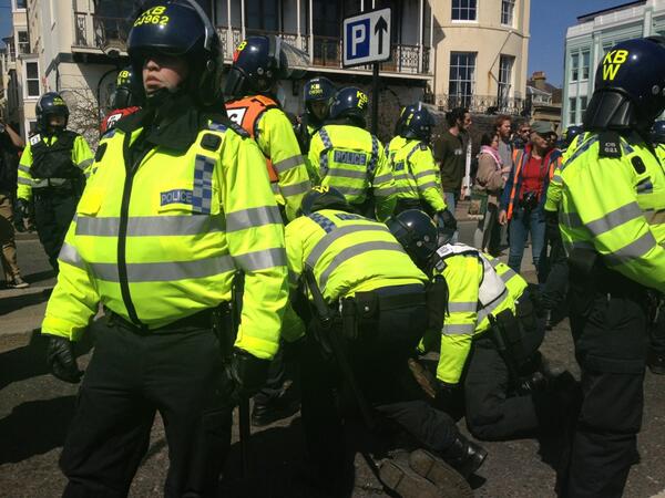 Cops forcefully unmasking people. Lots of cops on top of one skinny kid